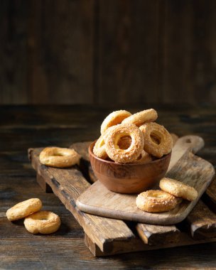 Kahverengi ahşap arka planda ahşap bir kaseye şeker serpiştirilmiş poğaça. Kurabiyelere yakın plan şeker serperim. Tatlı hamur işleri