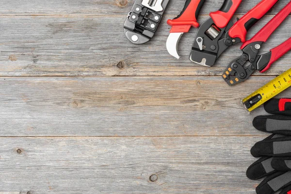 Tools of an electrician-fitter or Builder on a gray wooden table. Construction tools: crimps, knife, gloves and construction tape measure on the table. Top view with space for text