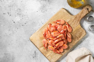 Açık gri mutfak masasında tahta tahtada karidesler. Servis kurulunda bir sürü karides var. Yukarıdan görünüşü