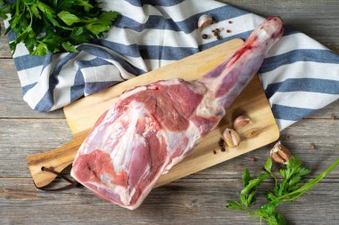 Gri ahşap bir masada tahta bir tahtanın üzerinde çiğ koyun bacağı. Yakın plan koyun eti. Masada taze bir kuzu eti var.