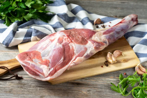 Raw mutton leg on a bone on a wooden Board on a gray wooden table. Sheep meat close-up. A fresh piece of lamb meat is on the table