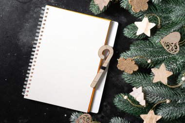 Mutlu yıllar ve mutlu Noeller. Noel ağacının dallarında ahşap süsler. Açık bir not defteri olan bir Noel arkaplanı. Noel Baba mektubu ya da hediye listesi kavramı