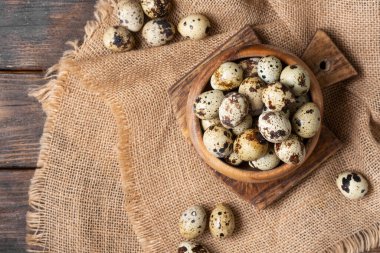 Kahverengi ahşap bir masada tahta bir kasede taze bıldırcın yumurtaları. Mutfak arka planında çiğ bıldırcın yumurtası. Yemek pişirmeye hazırlık kavramı. Metin için boşluk olan üst görünüm
