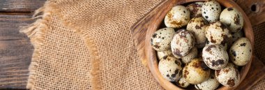 Kahverengi ahşap bir masada tahta bir kasede taze bıldırcın yumurtaları. Mutfak arka planında çiğ bıldırcın yumurtası. Yemek pişirmeye hazırlık kavramı. Metin için boşluk olan üst görünüm. Pankart