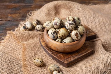 Kahverengi ahşap bir masada tahta bir kasede taze bıldırcın yumurtaları. Mutfak arka planında çiğ bıldırcın yumurtası. Yemek pişirme hazırlığı kavramı