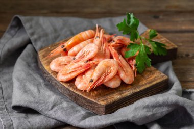 Kahverengi ahşap bir masanın üzerinde tahta bir tahta üzerinde karides. Servis kurulunda bir sürü karides var. Karidesler yaklaşıyor.