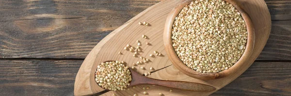 Green buckwheat in a wooden bowl on a brown wooden table. Superfood in a bowl. Green buckwheat close-up. The view from the top. Banner with space for text
