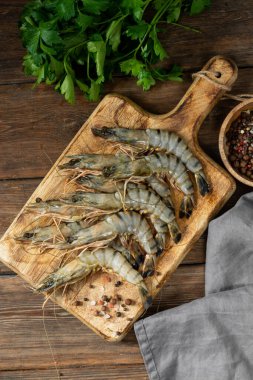 Kahverengi ahşap bir masada tahta servis tahtasında kaplan karidesleri. Bir sürü kaplan karidesi kapanıyor.