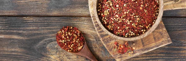 Spice mix: paprika, allspice, coriander, dried tomatoes. A mixture of various spices in a wooden bowl on a brown wooden kitchen table. Banner with space for text