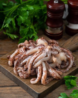 Mürekkep balıklarının dokunaçları. Kahverengi ahşap mutfak masasında ahşap servis tahtasında çiğ mürekkep balığı dokunaçları. Bir sürü mürekkep balığı dokunaçları