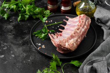 Genç bir kuzunun çiğ pirzolası. Siyah mutfak masasında siyah seramik tabakta çiğ kuzu kaburgası. Genç bir kuzunun çiğ eti masada.