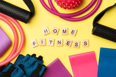 Evde fitness. Spor malzemelerinin arasında, sarı arka planda, tahta bloklara ev fitness yazılır. Sarı arka planda uygunluk için genişleticiler ve elastik bantlar