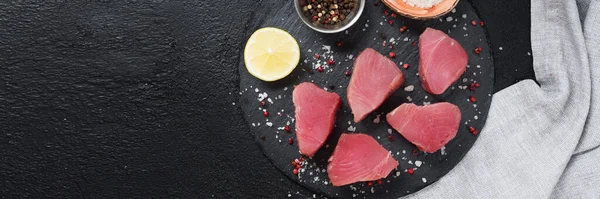 Raw tuna steaks on a black serving Board. Tuna fish on a Board on a black kitchen table. The view from the top. Banner with space for text