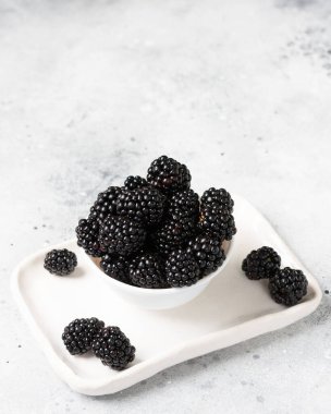 Böğürtlenler beyaz bir kasede, ışık masasının üzerinde. Yakın plan çekimde taze böğürtlen. Metin için boşluk