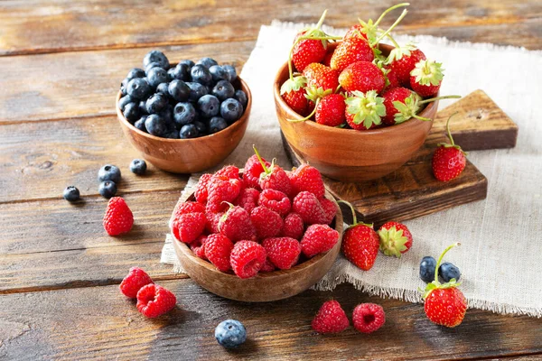 Berries. Various berries in wooden bowls on a brown wooden table. Strawberries, raspberries and blueberries in bowls