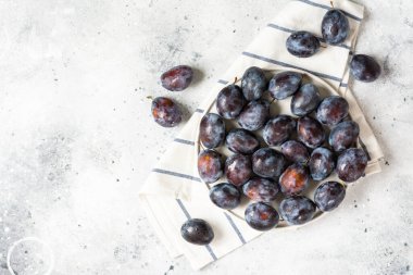 Olgun erik. Açık gri bir masada seramik tabakta bir sürü erik. Tabakta mavi erikler. Metin için boşluk olan üst görünüm. Sağlıklı meyve