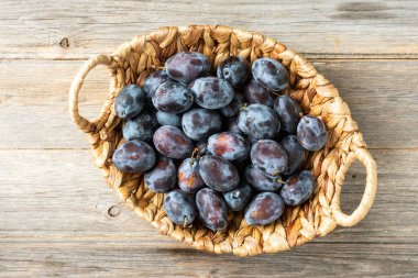 Olgun erik. Gri ahşap bir masada sepetin içinde bir sürü erik. Mavi erikler yakın plan. Yukarıdan manzara. Sağlıklı meyve