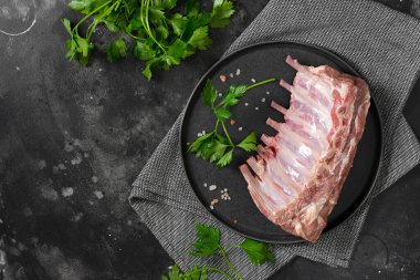 Genç bir kuzunun çiğ pirzolası. Siyah mutfak masasında siyah seramik tabakta çiğ kuzu kaburgası. Genç bir kuzunun çiğ eti masada.