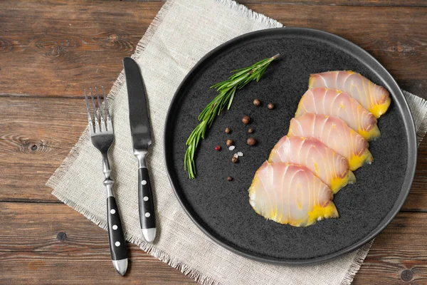 Cold-smoked sturgeon. Slices of sturgeon fish in a black ceramic plate on a brown wooden table