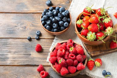 Böğürtlen Kahverengi ahşap bir masada ahşap kaselerde çeşitli meyveler. Çilek, ahududu ve yaban mersini kaselerinde
