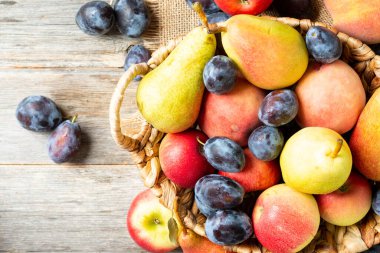 Masadaki sepetin içinde meyve çeşitleri. Sepette bir sürü farklı çiğ meyve var. Erikler, şeftaliler, elmalar ve armutlar masada. Sağlıklı beslenme. Metin için boşluk olan üst görünüm