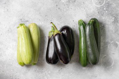 Çiğ kabak ve patlıcan. Açık gri bir masada kabak ve patlıcan. Metin için boşluk olan üst görünüm. Kabak ve patlıcan hasadı