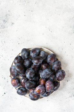 Olgun erik. Açık gri bir masada seramik tabakta bir sürü erik. Tabakta mavi erikler. Metin için boşluk olan üst görünüm. Sağlıklı meyve