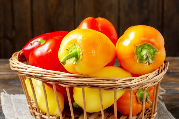 Bell pepper. Red, yellow and orange peppers in a basket on a brown wooden table. Paprika close up