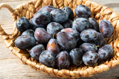 Olgun erik. Gri ahşap bir masada sepetin içinde bir sürü erik. Mavi erikler yakın plan. Sağlıklı meyve