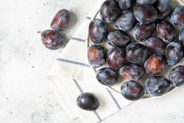 Olgun erik. Açık gri bir masada seramik tabakta bir sürü erik. Tabakta mavi erikler. Metin için boşluk olan üst görünüm. Sağlıklı meyve