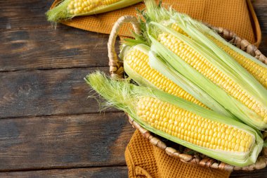 Mısır. Kahverengi ahşap bir masada sepetteki taze çiğ mısır. Sonbahar hasadı konsepti