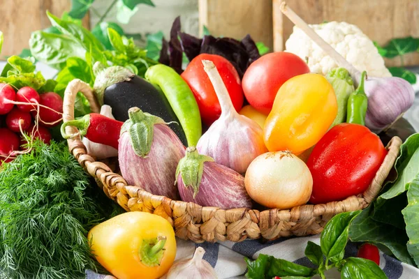 Assortment of vegetables in a basket on the table. A lot of different raw vegetables in the basket. Eggplant, tomatoes, garlic, sweet pepper, onion on the table. Healthy food concept