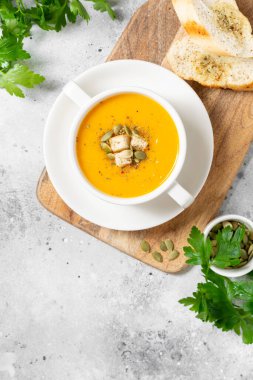 Balkabağı çorbası. Açık gri mutfak masasında beyaz tabakta balkabağı kremalı çorba. Vejetaryen sonbahar çorbası. Yukarıdan görünüşü