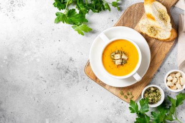 Balkabağı çorbası. Açık gri mutfak masasında beyaz tabakta balkabağı kremalı çorba. Vejetaryen sonbahar çorbası. Yukarıdan görünüşü