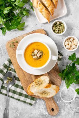 Balkabağı çorbası. Açık gri mutfak masasında beyaz tabakta balkabağı kremalı çorba. Vejetaryen sonbahar çorbası. Yukarıdan görünüşü