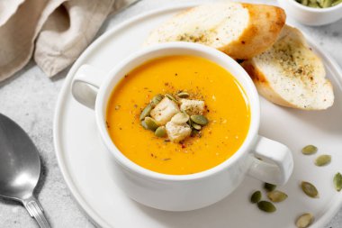 Balkabağı çorbası. Açık gri mutfak masasında beyaz tabakta balkabağı kremalı çorba. Vejetaryen sonbahar çorbası yakın plan.