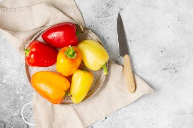 Tatlı biber. Açık gri mutfak masasında seramik bir kasede kırmızı, sarı ve turuncu biberler. Metin için boşluk olan üst görünüm
