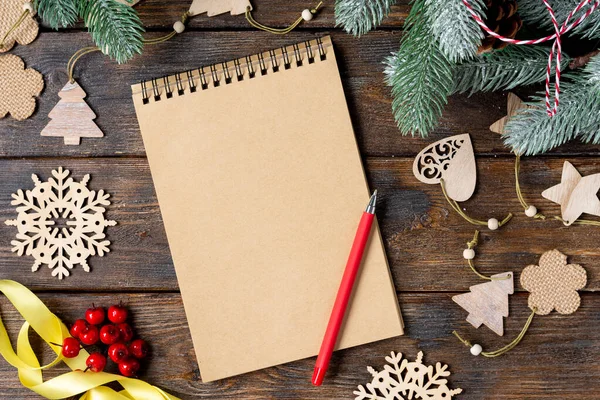 Mutlu yıllar ve mutlu Noeller. Noel ağacının dallarında ahşap süsler. Açık bir not defteri olan bir Noel arkaplanı. Noel Baba mektubu ya da hediye listesi kavramı