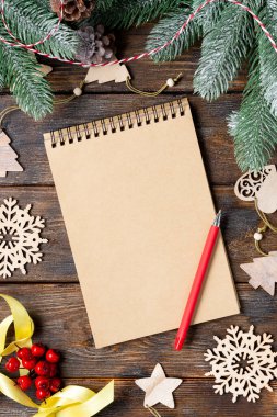 Mutlu yıllar ve mutlu Noeller. Noel ağacının dallarında ahşap süsler. Açık bir not defteri olan bir Noel arkaplanı. Noel Baba mektubu ya da hediye listesi kavramı