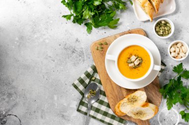 Balkabağı çorbası. Açık gri mutfak masasında beyaz tabakta balkabağı kremalı çorba. Vejetaryen sonbahar çorbası. Metin için boşluk olan üst görünüm