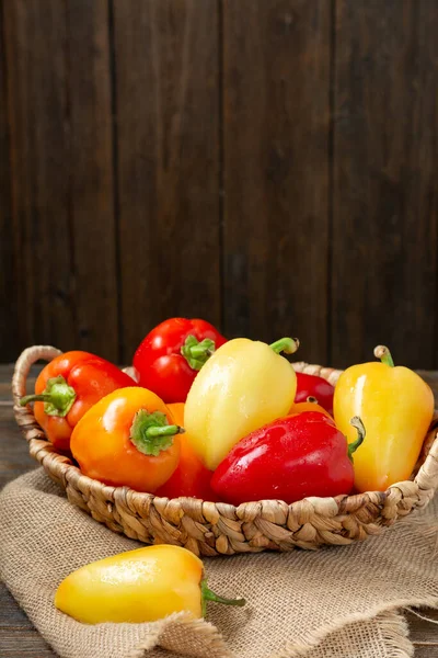 Sweet pepper. Red, yellow and orange peppers in a basket on a brown wooden table. Paprika close up