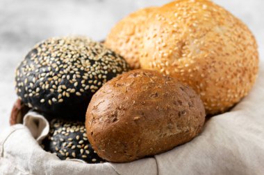 Hamburger için susamlı çörek. Açık gri arka planda bir sepette buğday ve çavdar ekmeği. Susamlı ev yapımı çörekler. Yakın çekim pişiriliyor.