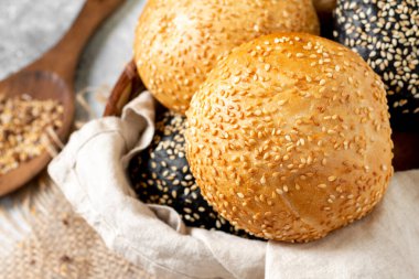 Hamburger için susamlı çörek. Açık gri arka planda bir sepette buğday ve çavdar ekmeği. Susamlı ev yapımı çörekler. Yakın çekim pişiriliyor.