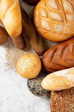 Buğday ve çavdar ekmeği. Açık gri bir masada farklı şekillerde çavdar ve buğday ekmeği. Bagetler, somunlar, yuvarlak ekmek, çörekler ve hamburgerler masada. Üst Manzara. Kopyalama. Pankart