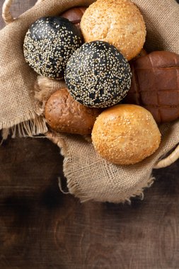 Hamburger için susamlı çörek. Buğday ve çavdar kahverengi ahşap arka planda bir sepette yuvarlanır. Susamlı ev yapımı çörekler. Yukarıdan manzara. Kopyalama alanı