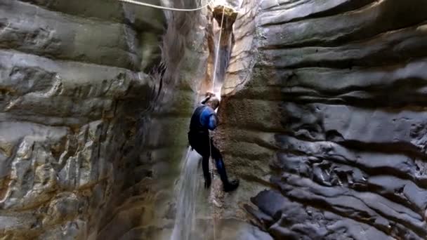 滝のラッピング。濡ったスーツを着た男が狭い川の渓谷の滝に登る — ストック動画