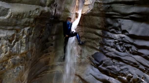 Репеллинг водопада. Человек в мокром костюме взбирается на водопад в узком речном каньоне — стоковое видео