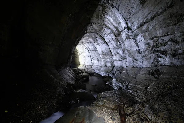 Underground river flowing through large oviform underground turning sewer tunnel — Stock Photo, Image