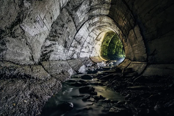 Underground river flowing through large oviform underground turning drainage sewer tunnel — Stock Photo, Image