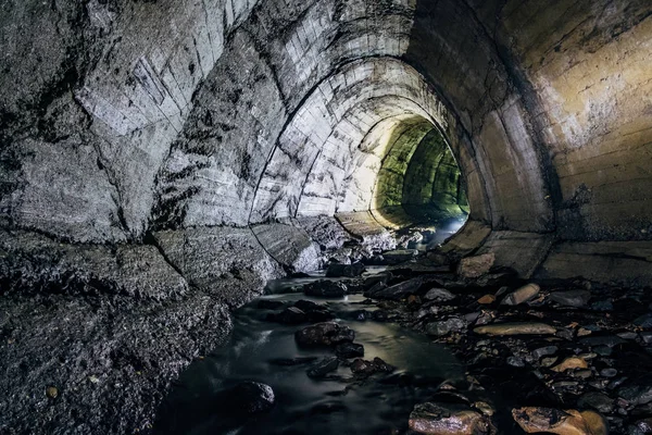 Underground river flowing through large oviform underground turning drainage sewer tunnel